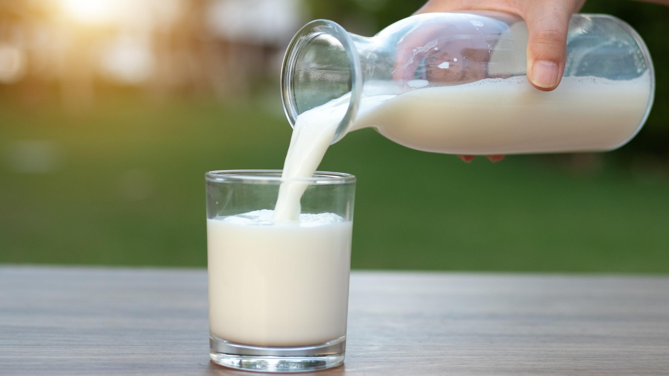 hand pouring milk in a glass against a nature background